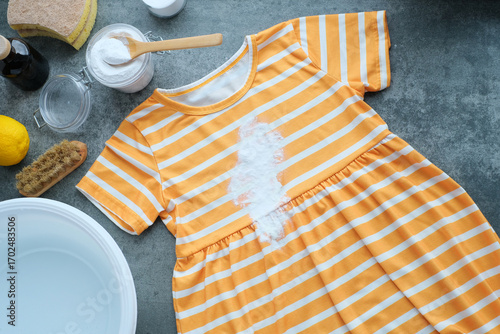 White baking soda powder sprinkled on the stain for environmentally friendly stain removal. Spilled cosmetic stains a yellow striped dress lies on a gray surface. Natural cleaning products. Zero waste