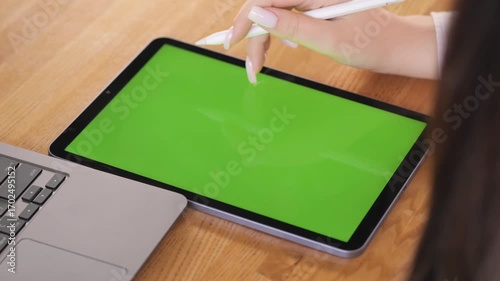 Green tablet is on a wooden table. A laptop is on the table next to the tablet