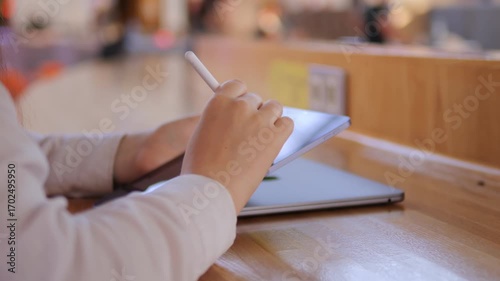 Person is using a tablet on a wooden table. The tablet is open and the person is typing on it