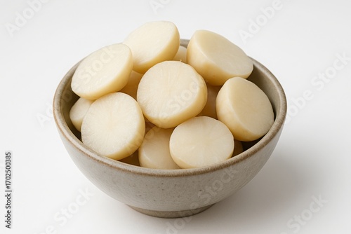Bowl filled with peeled and sliced water chestnuts on a white background.