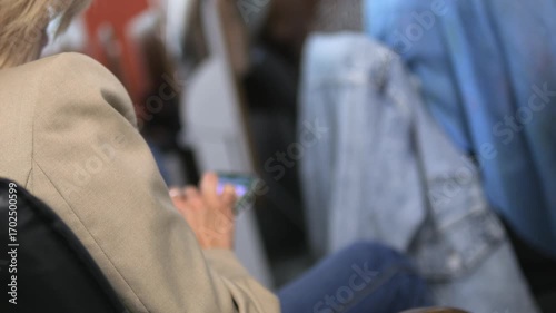 Woman is sitting on a chair and using her cell phone. A backpack is on the floor in front of her
