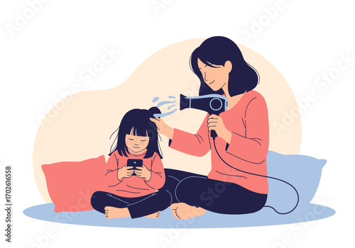 Mother drying her daughter's hair while the child is engrossed in her smartphone device
