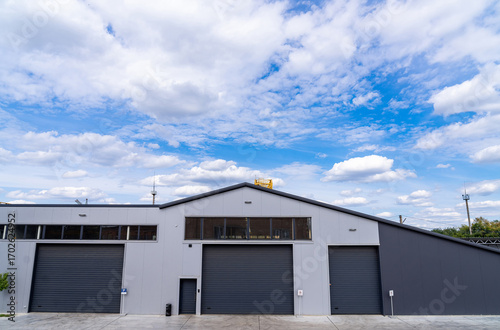 Wallpaper Mural Modern warehouse under cloudy sky in urban setting. Large warehouse building situated in a city, featuring multiple garage doors and a bright blue sky with clouds. Torontodigital.ca