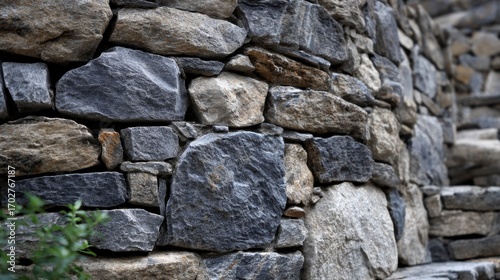 A stone wall constructed from irregular grey and beige stones with green foliage at the bottom left