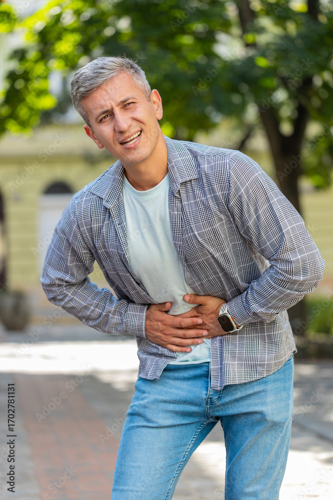 Obraz premium Caucasian man traveler feeling sudden strong abdominal stomach ache, gastritis problem. Upset tourist having symptom poisoning diarrhea indigestion peptic ulcer pancreatitis on city street. Vertical.
