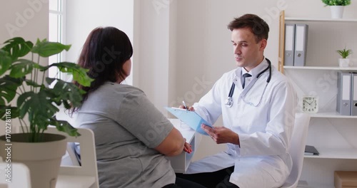 Male physician or cardiologist giving consultation to overweight fat female patient in clinic about wellness, nutrition, weight loss, answering questions, giving advices and describing treatment plan.
