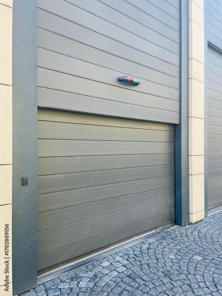 Fototapeta premium On a picturesque cobblestone street, a gray garage door stands wide open, allowing glimpses of the interior within