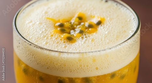 Close up of a passion fruit cocktail with foam in a clear glass on a brown table