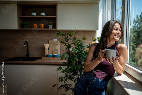 Photography Young woman enjoying a cup of coffee by the window in a modern kitchen