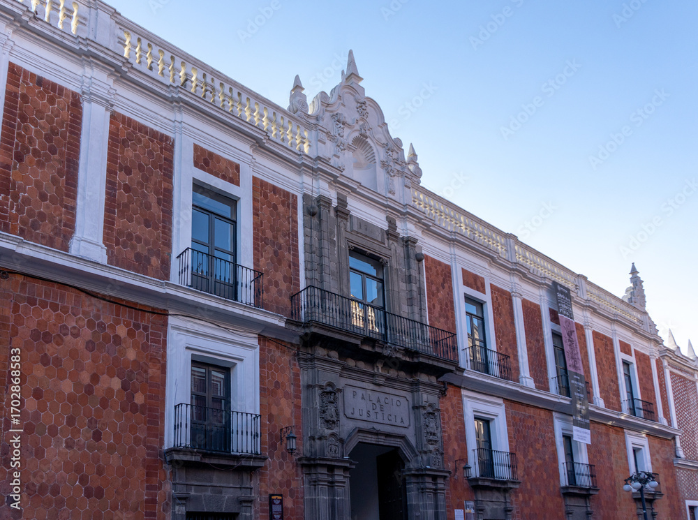 Fototapeta premium A large building with a red brick facade and white trim. The building has a balcony and a large window. City of Puebla, Mexico, crafts