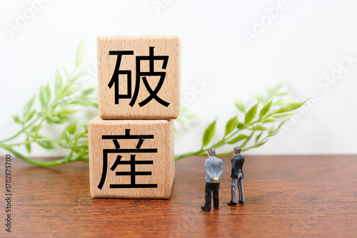 木製ブロックに破産の文字とミニチュアのビジネスマンのイメージ