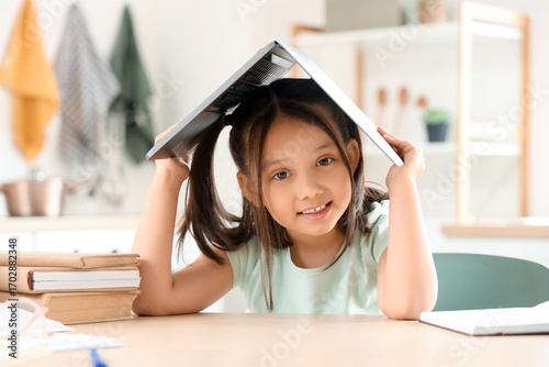 Little Asian girl with laptop at table in kitchen