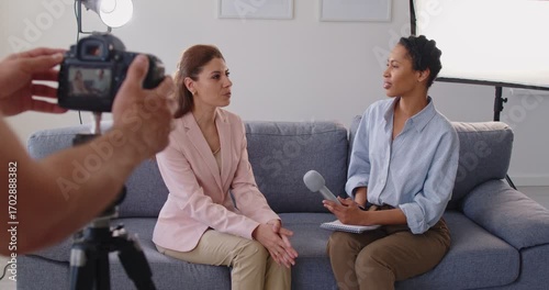 African american female journalist interviewing woman sitting on sofa in studio talking with each other shooting live video. Digital camera recording podcast video interview. 4k video.