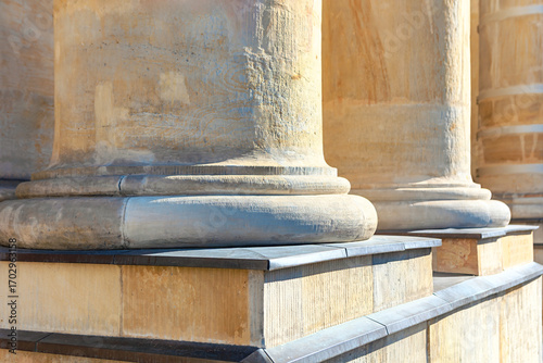 Weathered stone bases of several large columns. Sunlight creates shadows and rough texture and classical architecture. Enduring strength of stone is evident in detailed base of classical column