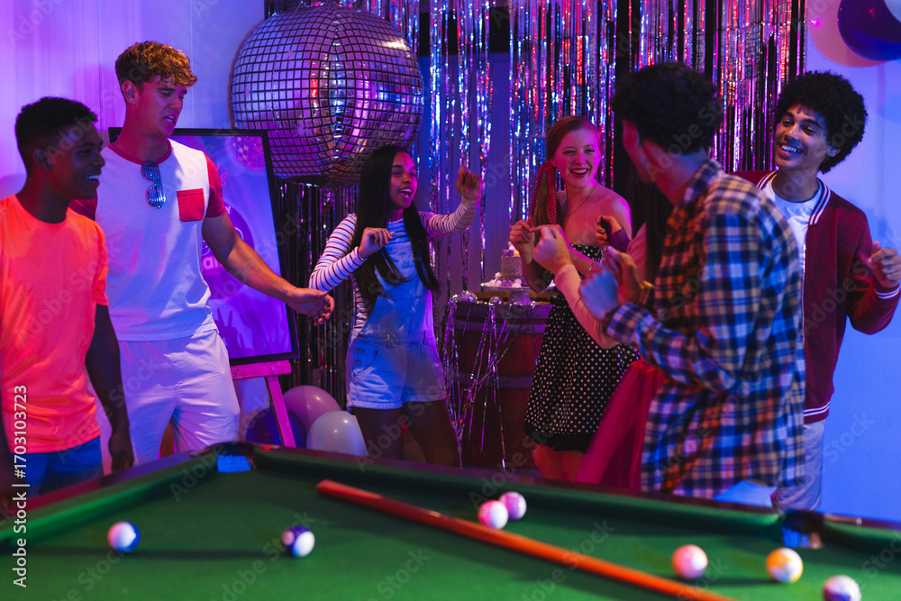 Obraz premium Teens celebrating around pool table with disco ball and festive decorations