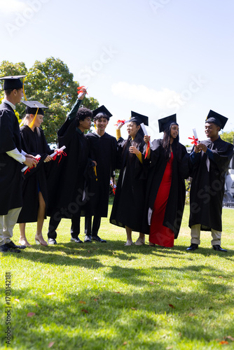Graduating students in caps and gowns celebrating with diplomas on sunny day