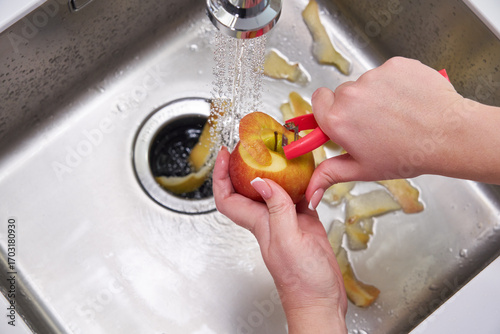 Fototapeta Cropped view of female hands peeling apple over Food waste disposer machine
