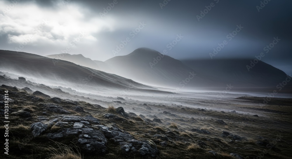Fototapeta premium Misty mountains shrouded in atmospheric fog and low clouds, with rugged terrain in the foreground.