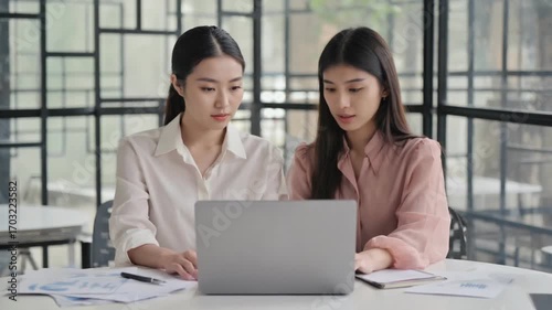 Focused Collaboration: Two women intently focused on a laptop, immersed in a shared project or work task in a modern, bright setting. 