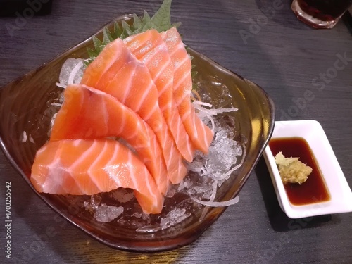 Exquisite Salmon Sashimi: The vibrant image showcases a meticulously arranged plate of fresh, raw salmon sashimi, presented alongside a delicate garnish and a dipping sauce, a culinary delight.