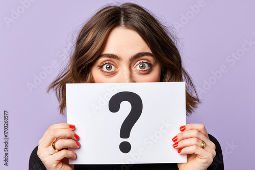 Young woman with wide eyes holding a white card displaying a large black question mark against a purple background