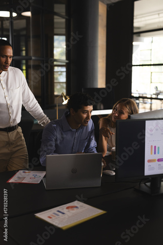 Collaborating on project, business professionals using laptop and charts in office