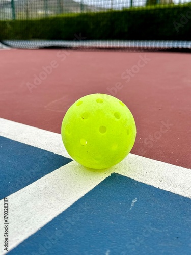 Pickleball ball close up on the hard surface by the net.  Yellow perforated, hollow plastic ball for pickleball sport 
