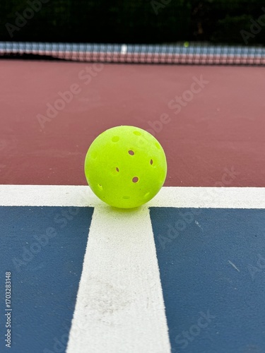 Pickleball ball close up on the hard surface by the net.  Yellow perforated, hollow plastic ball for pickleball sport 