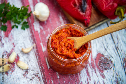 Close-up of two slices of bread topped with vibrant homemade ajvar on a rustic wooden table.