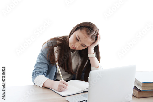 Serious Caucasian girl learning online with laptop and writing homework on notebook in classroom of school. Education cancept