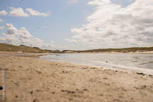 Fotografija Sandy beach under a sunny sky with gentle waves washing ashore in a coastal land