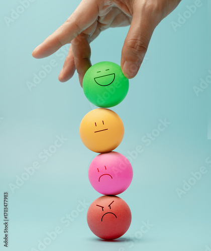 Hand balancing Colorful emotional faces Ball, symbolizing mental health and emotional self-regulation through balancing positive and negative emotions