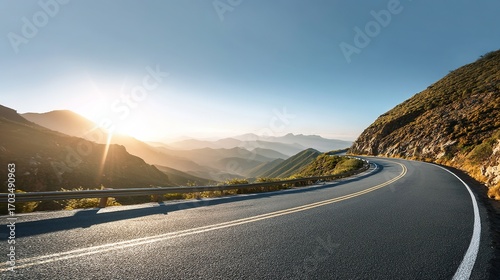 Curved asphalt road winding through lush mountains, bathed in glowing sunlight that adds warmth to the scene, with plenty of copy space in the sky for text, logos, or design elements.