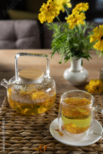 Bright herbal tea with flowers in a cozy indoor setting near a vase of yellow blooms on a woven placemat