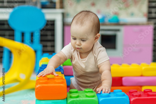 Baby exploring colorful toy building blocks indoors. Sensory experience