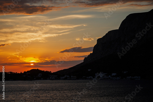Scenic view of orange sky, the village and silhouette of the steep Telendos island in Greece at sunset.