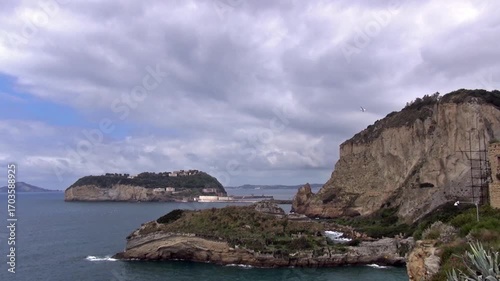 Coastline facing the island of Nisida in the Gulf of Naples with a gull hovering above. Inlet adjacent to Trentaremi (thirty oars) Bay a Dente di Cane (Tooth’s dog) cliff. Posillipo, Naples, Italy.