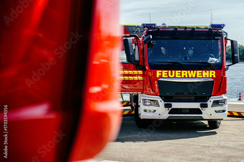 Frontansicht eines modernen Feuerwehrfahrzeugs. Unscharfes Einsatzfahrzeug im Vordergrund. Symbolisiert Einsatzbereitschaft, Katastrophenschutz und schnelle Hilfe.