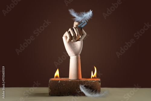 Contemporary still life: a wooden hand holds a blade on which a feather is balanced. Conceptual photography, freekbana with fire special effects.