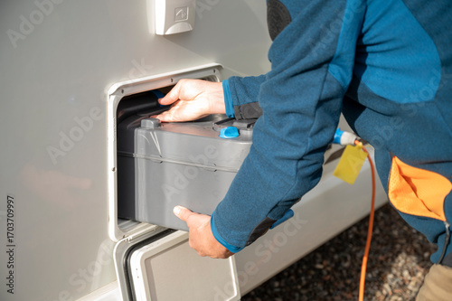 Person placing cassette toilet waste tank into camper van compartment during outdoor sanitation routine