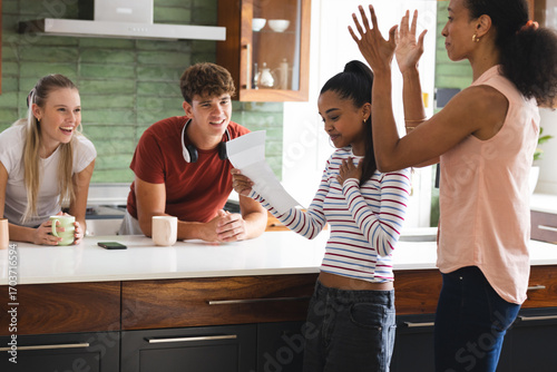 Teens celebrating good news in kitchen, reading letter with excitement and joy
