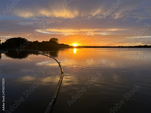 Summer sunset landscape sun setting over Norfolk Broads England uk tranquil water with the beautiful orange yellow blue skies viewed from sailing boat to horizon and trees reeds, clouds reflected 