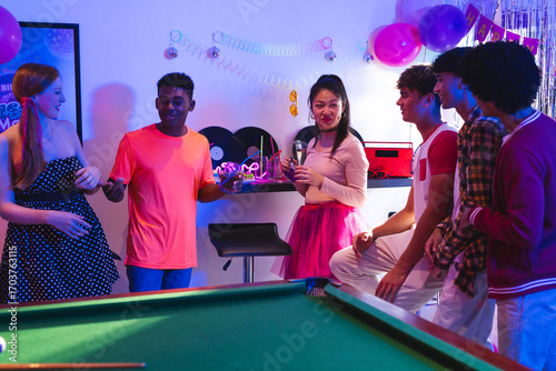 Teenagers enjoying lively party with drinks and laughter around pool table