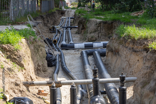 Urban construction site with large black water pipes laid in a trench during city infrastructure repair and replacement. Maintenance, engineering, modernization and municipal development