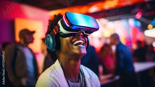 A young man wearing a VR headset and headphones, standing in a brightly lit room with colorful lights and a blurred background.