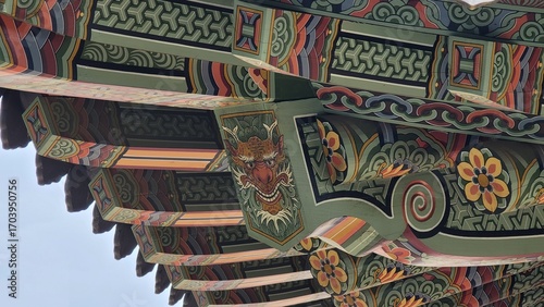 Traditional Korean temple architecture with vibrant dancheong patterns on eaves and roofs, showcasing colorful wooden details against blue sky and nature.