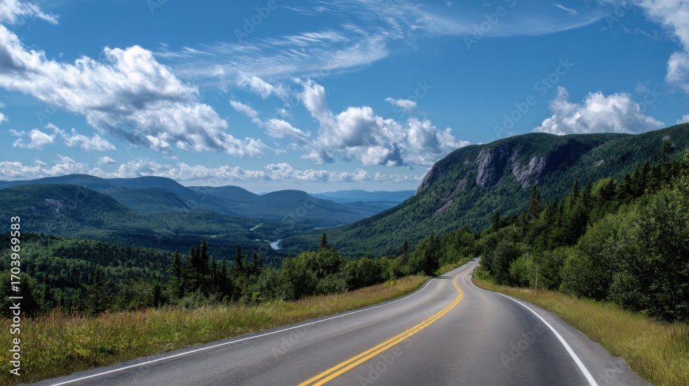Fototapeta premium A winding road stretches through vibrant green hills and valleys, showcasing natures beauty. Fluffy clouds float across the clear blue sky on a warm summer day, inviting adventure.