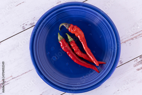 3 red hot chili peppers on a blue plate against a white-washed distressed wood surface.
