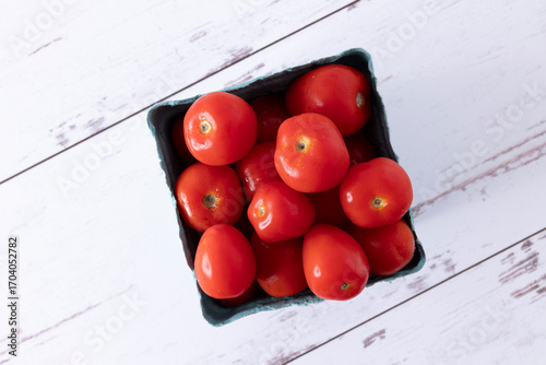 Pint of strawmato variety tomatoes, with water droplets, on white-washed distressed wood surface.