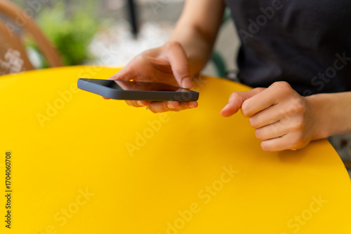 Close-up mid section of a man sitting at a yellow garden table using a mobile phone in summer